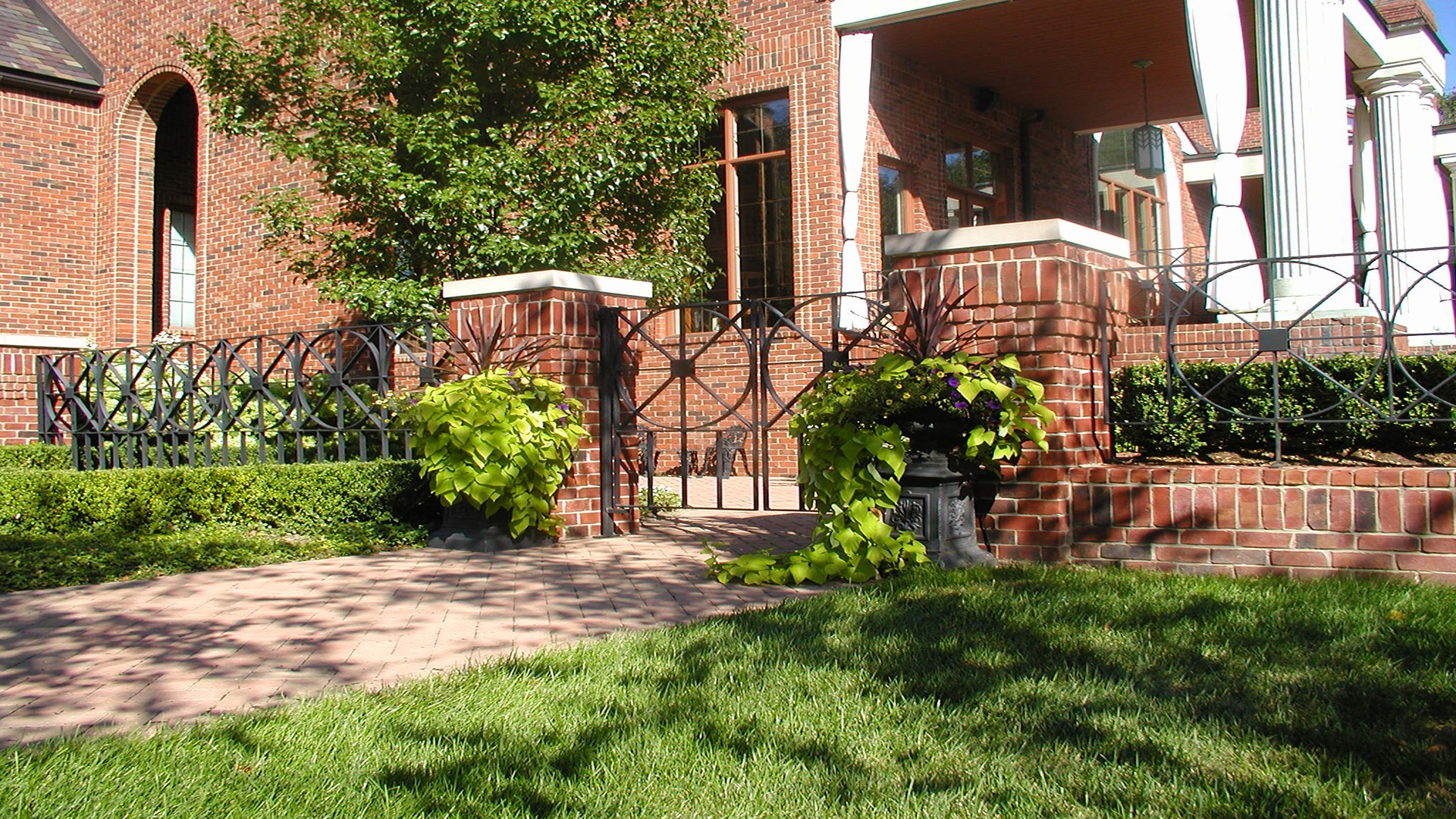 A red brick building with a black iron gate, lush greenery, and a well-maintained lawn, showcasing classic architectural elements and inviting entrance.