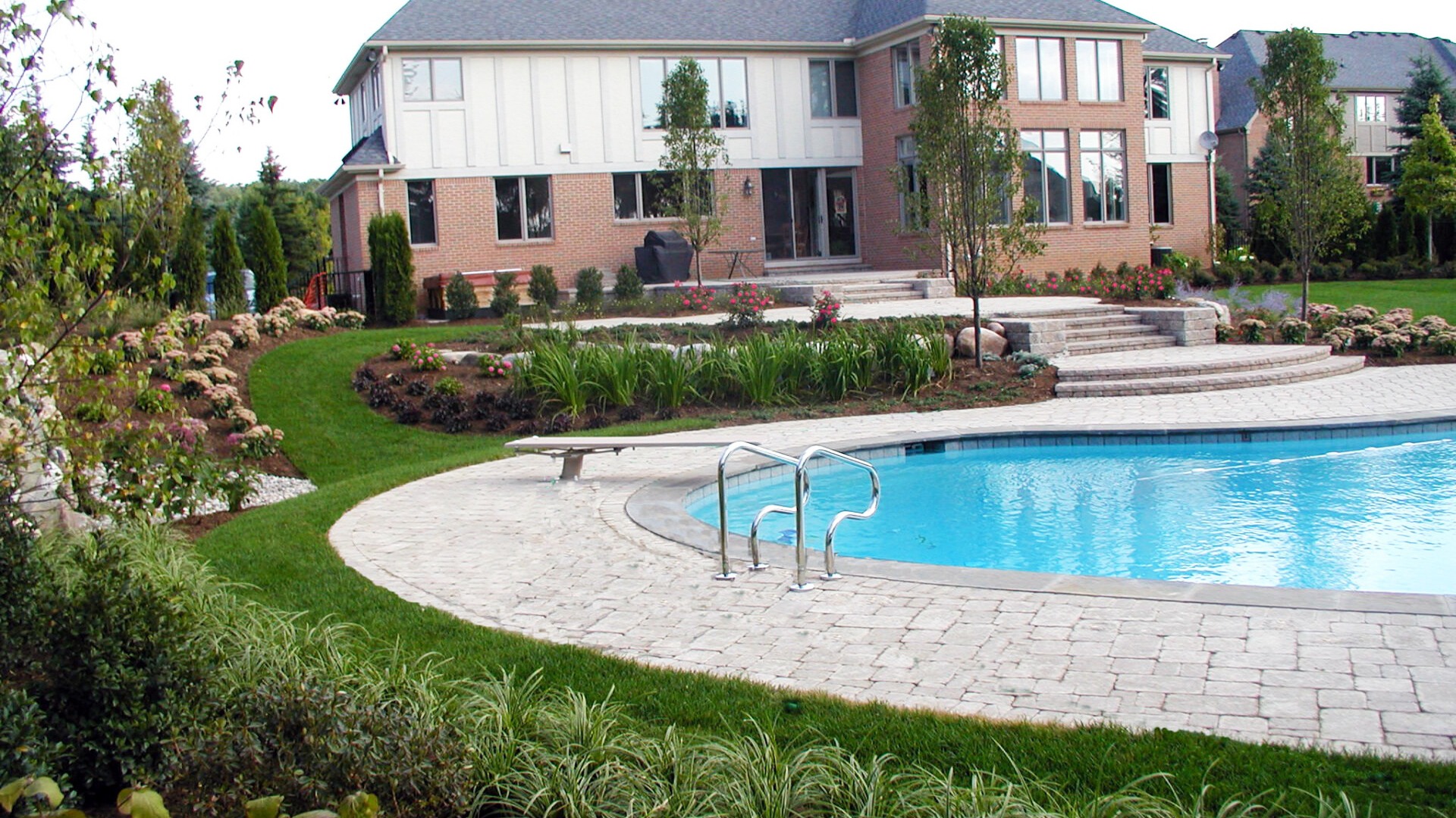 A brick house with large windows overlooks a landscaped backyard featuring a kidney-shaped swimming pool and manicured gardens.