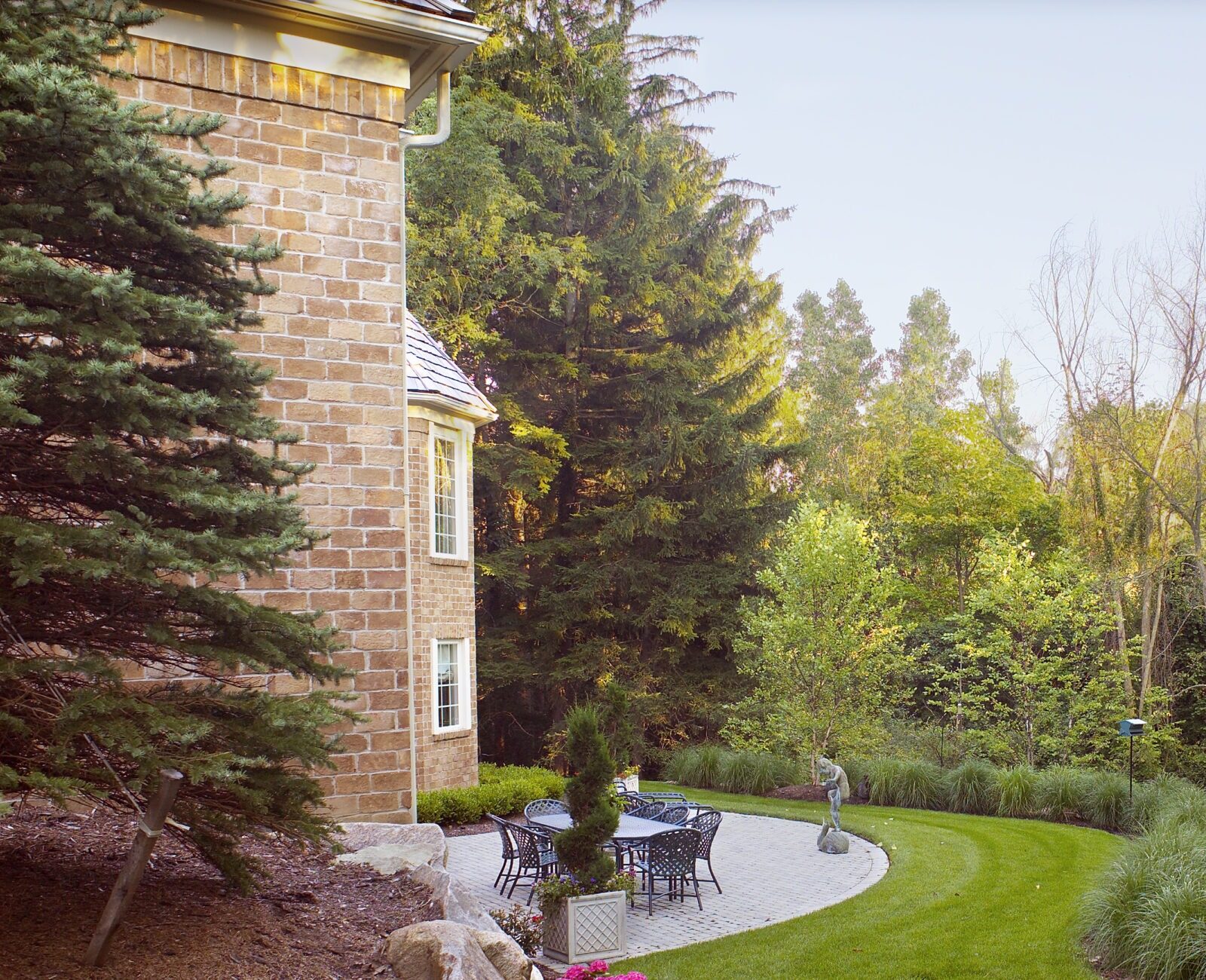Brick house with patio furniture, surrounded by lush greenery and mature trees. Well-maintained lawn and landscaping create a tranquil, inviting outdoor space.