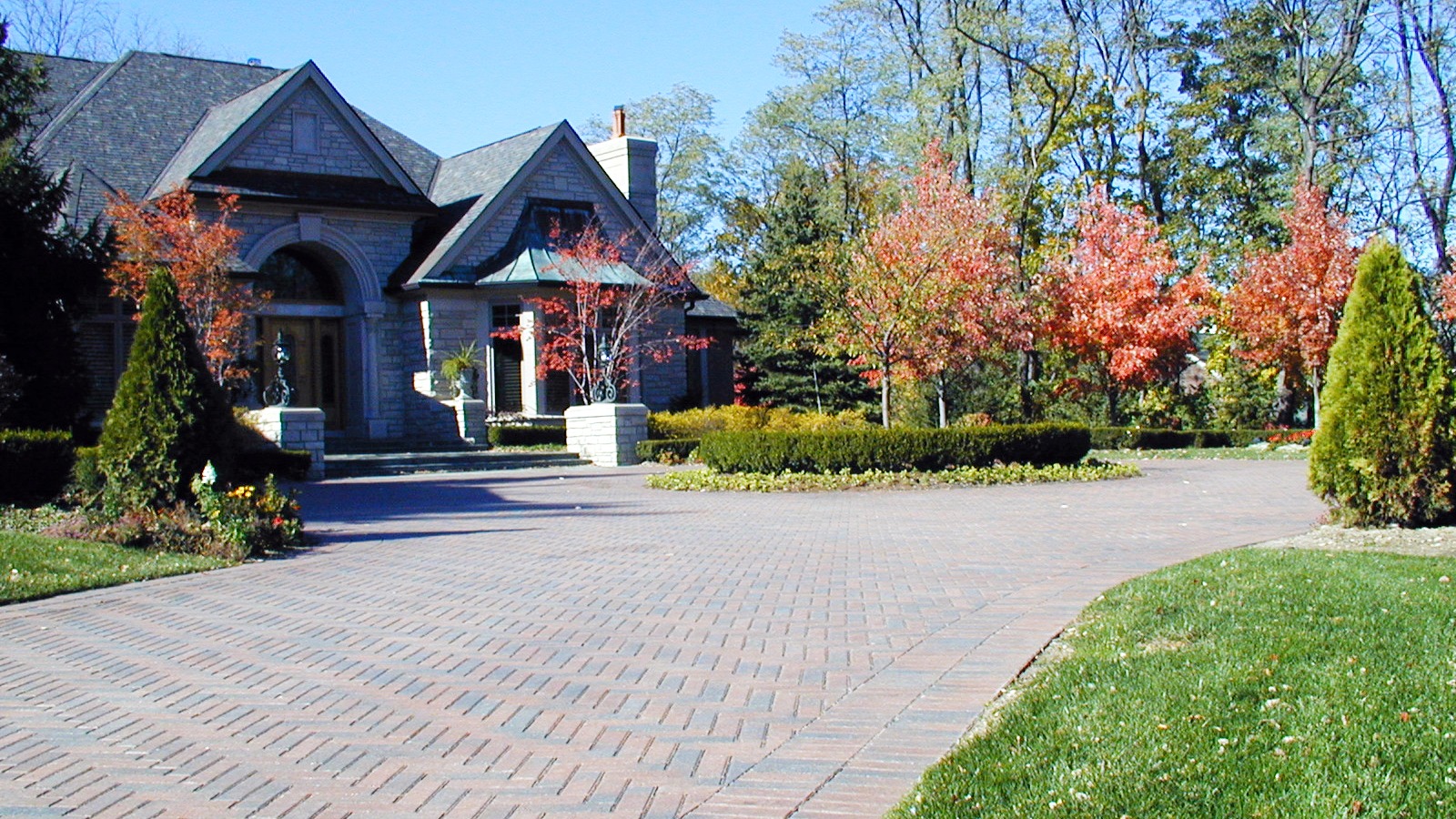 A large house surrounded by vibrant autumn trees and a paved driveway. The scene is peaceful and well-maintained, conveying a sense of tranquility.