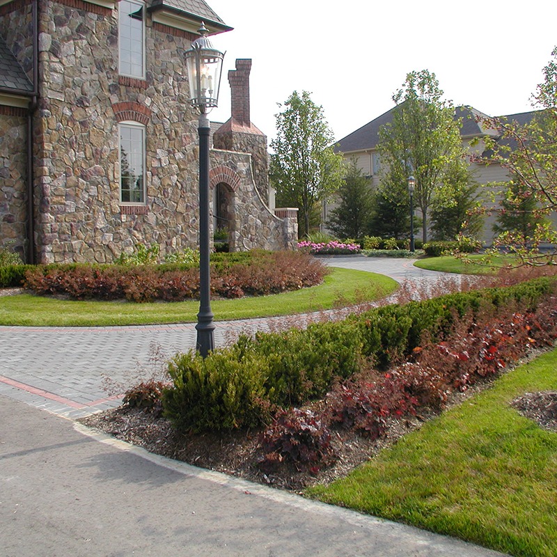 A stone house with a landscaped garden, pathway, and vintage-style lamppost. Well-maintained hedges and trees surround the area, creating a serene atmosphere.
