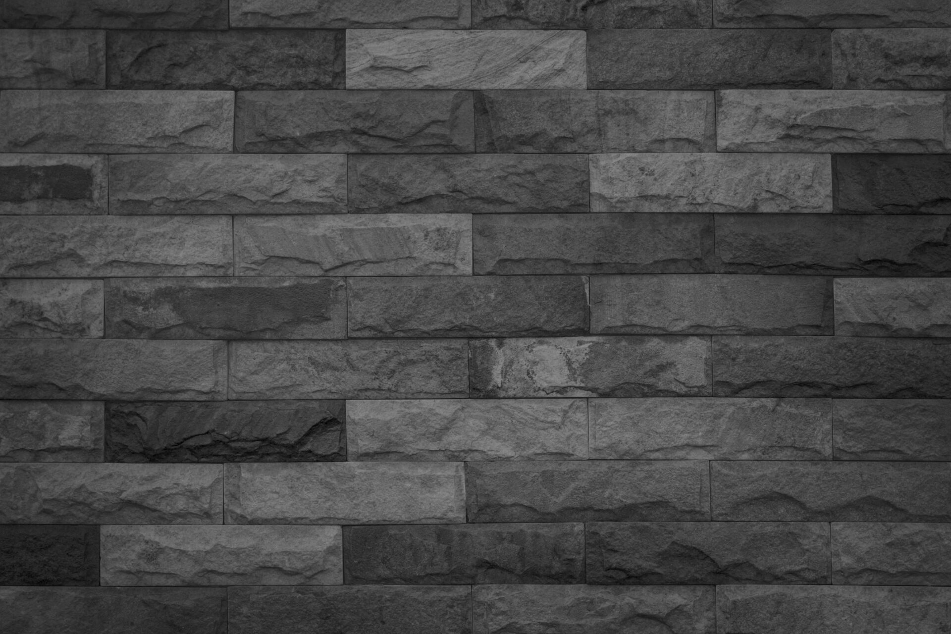 Close-up of a textured, gray brick wall with uneven surfaces and a uniform rectangular pattern, creating a rustic, industrial appearance.