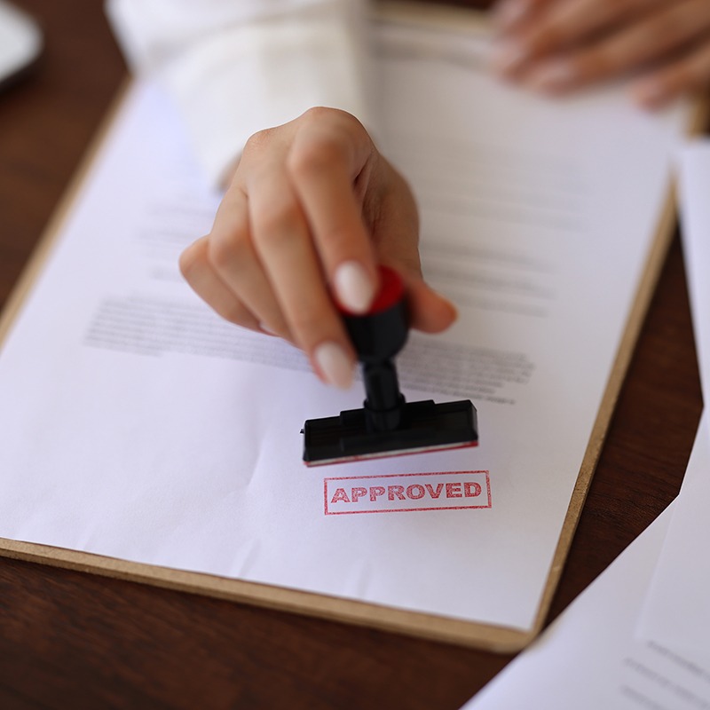 A person stamps "APPROVED" on a document, signifying approval or authorization on a clipboard containing official papers.