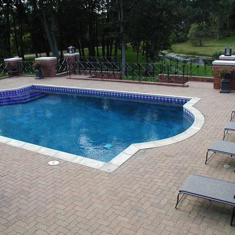 A serene outdoor pool surrounded by brick patio, lounge chairs, and lush greenery, set in a tranquil garden atmosphere with distant trees.