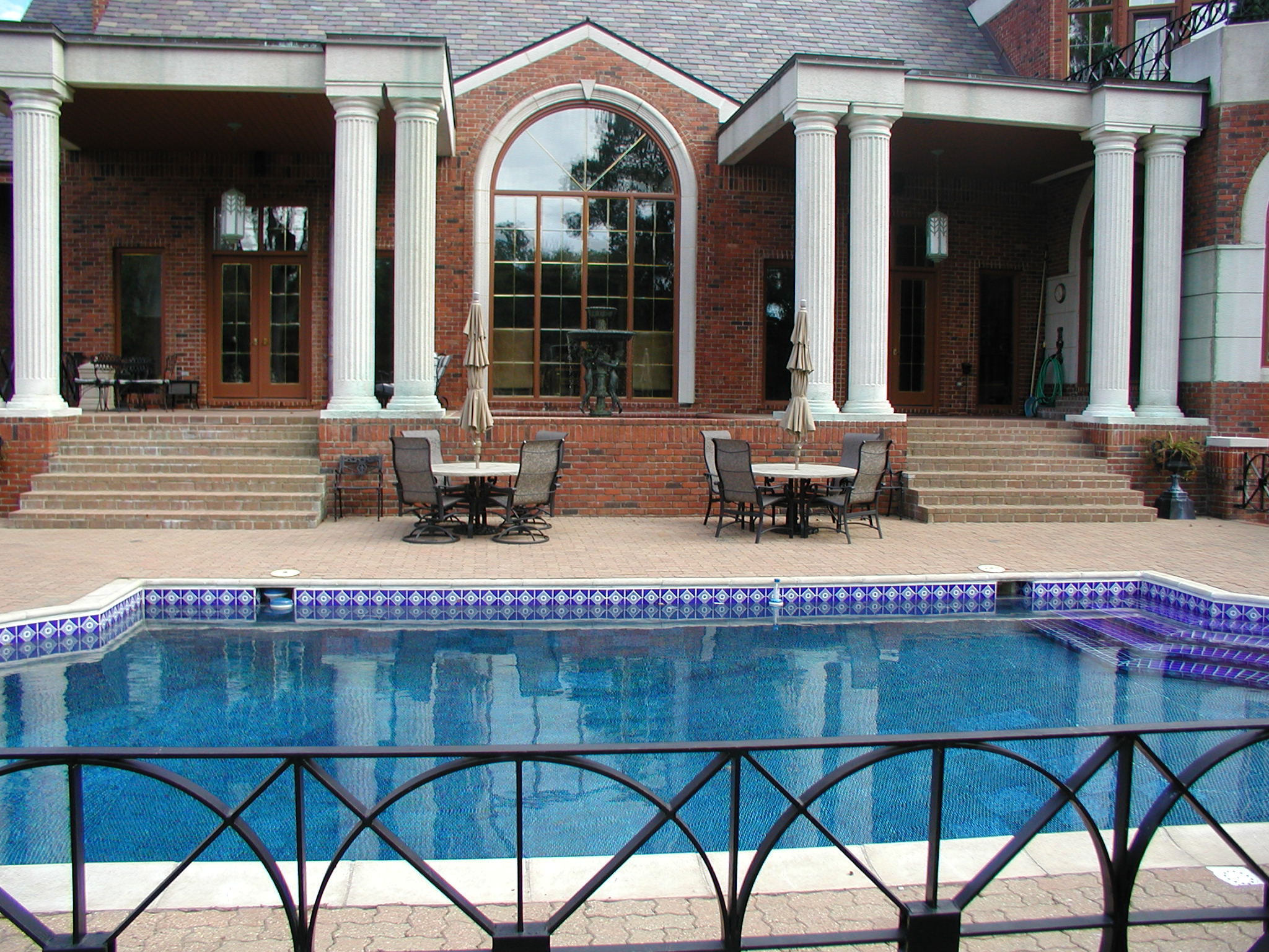 Elegant house with brick exterior, tall white columns, and large windows. A swimming pool and patio furniture enhance the outdoor space.