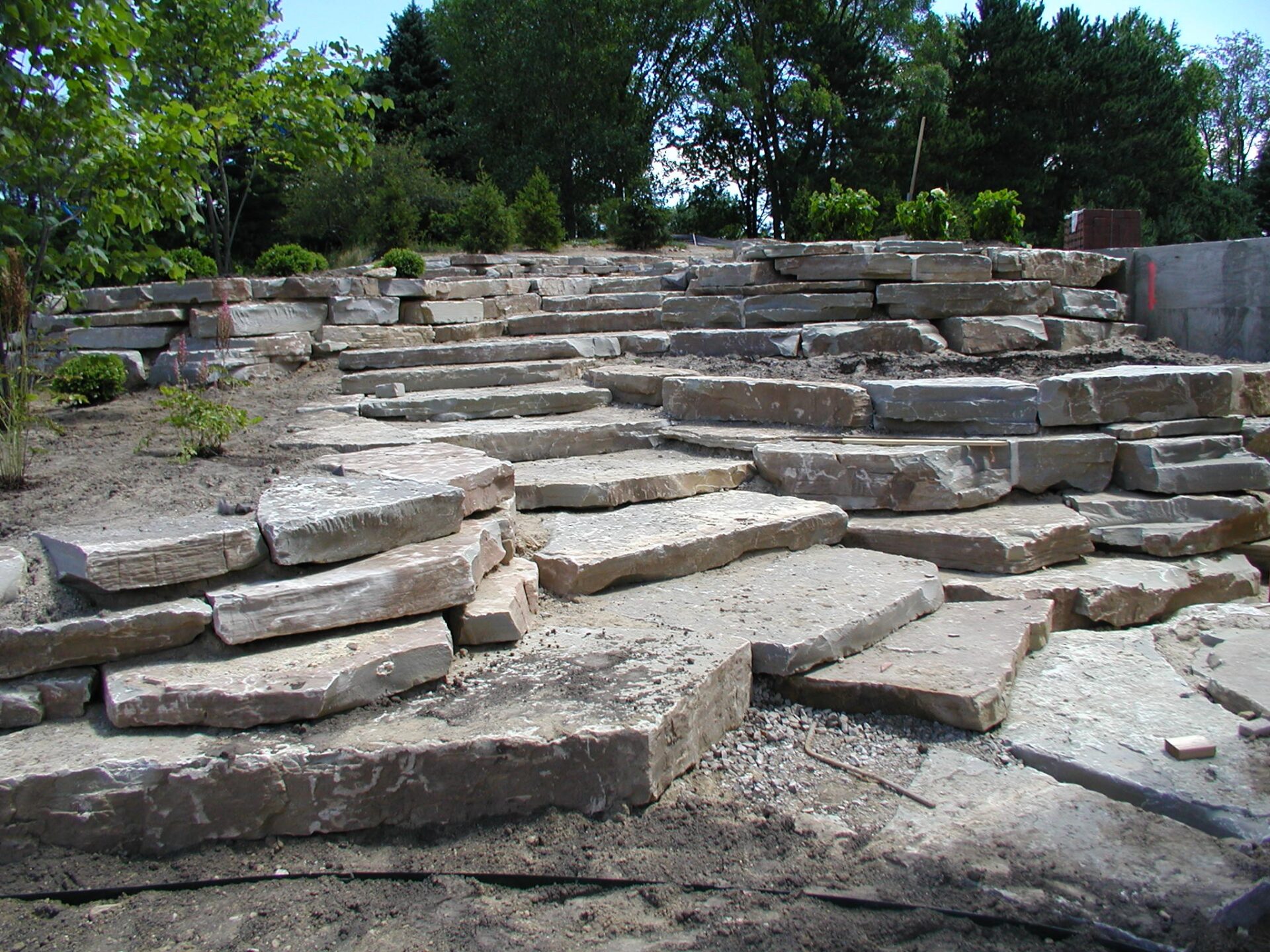 Natural stone steps arranged in a garden setting, surrounded by lush greenery and trees, creating a rustic outdoor landscape feature.
