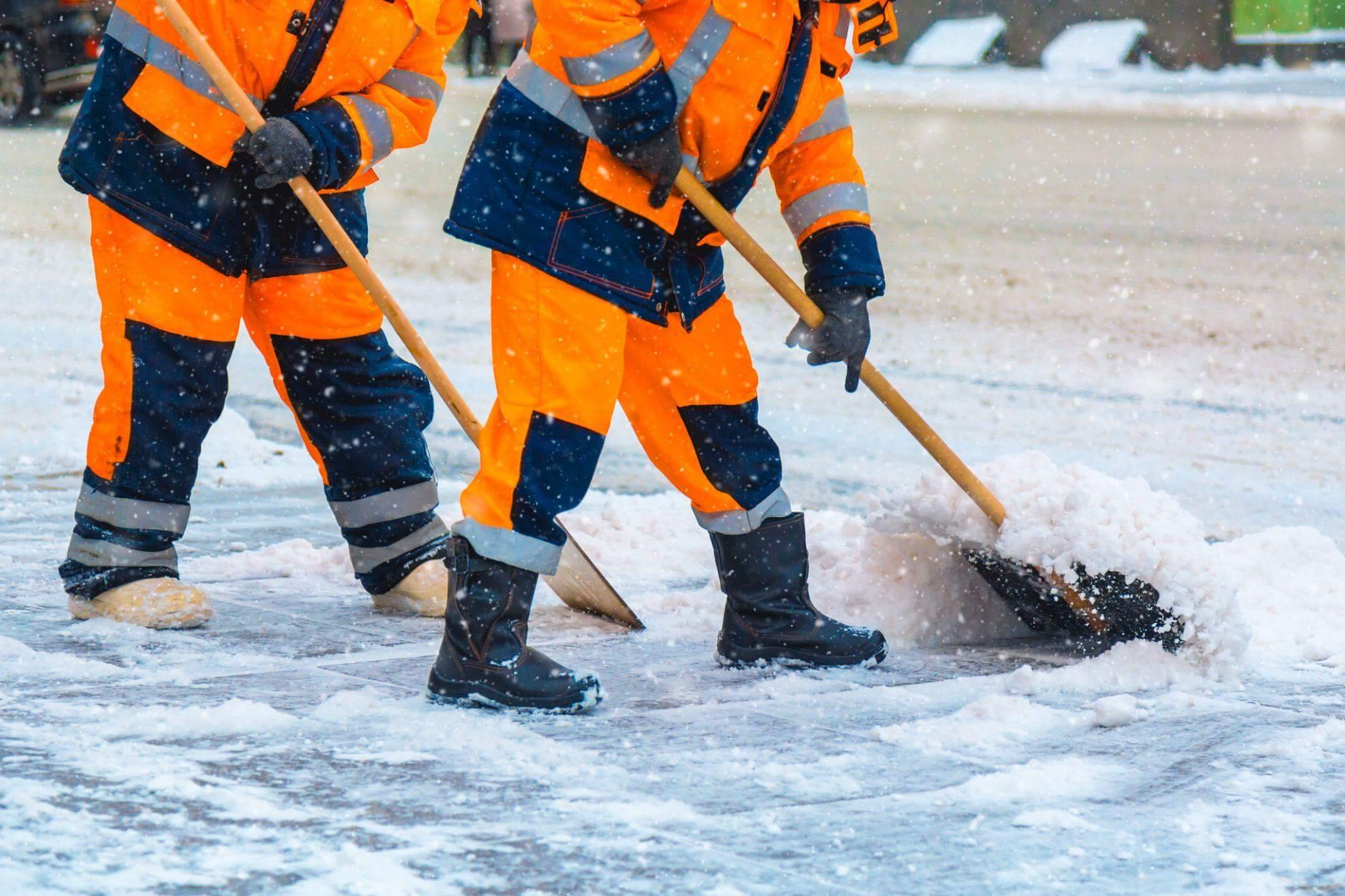 Men in orange jackets cleaning snow on a commercial property