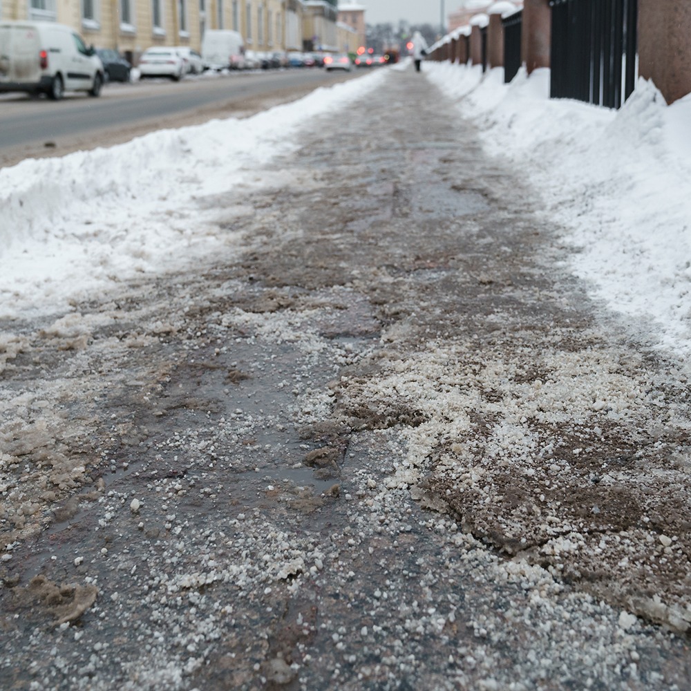Closeup of technical salt grains on icy sidewalk surface in winter, used for melting ice and snow.